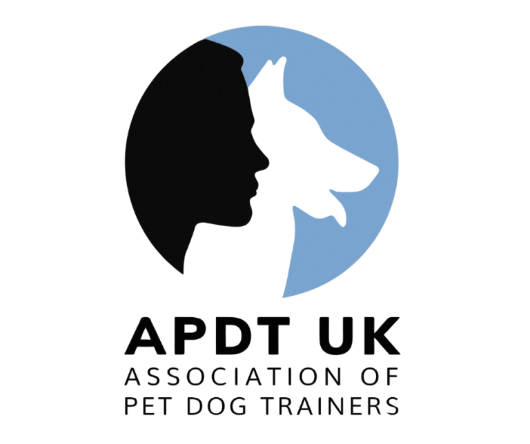 Logo featuring a circular emblem set against a blue background, depicting a black silhouette profile of a human face side-by-side with a white silhouette profile of a dog's head looking upward with its tongue out. Below the emblem, bold black text reads "APDT UK", followed by the words "ASSOCIATION OF PET DOG TRAINERS" stacked underneath in a smaller uppercase font.
