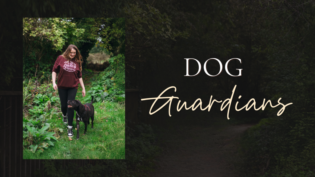 On the left, a vertical inset photo shows a smiling woman wearing a maroon long-sleeve top and black pants walking along a grassy, tree-lined path alongside a black dog. The right side features a dark, soft-focus background of trees overlaid with large text reading "DOG" in a clean, white serif font and "Guardians" in a cursive, handwriting-style script.